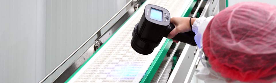 Handgehaltener UV Scanner BioDtex macht Verunreinigungen & Biofilme auf einem Fließband in der Lebensmittelproduktion sichtbar.